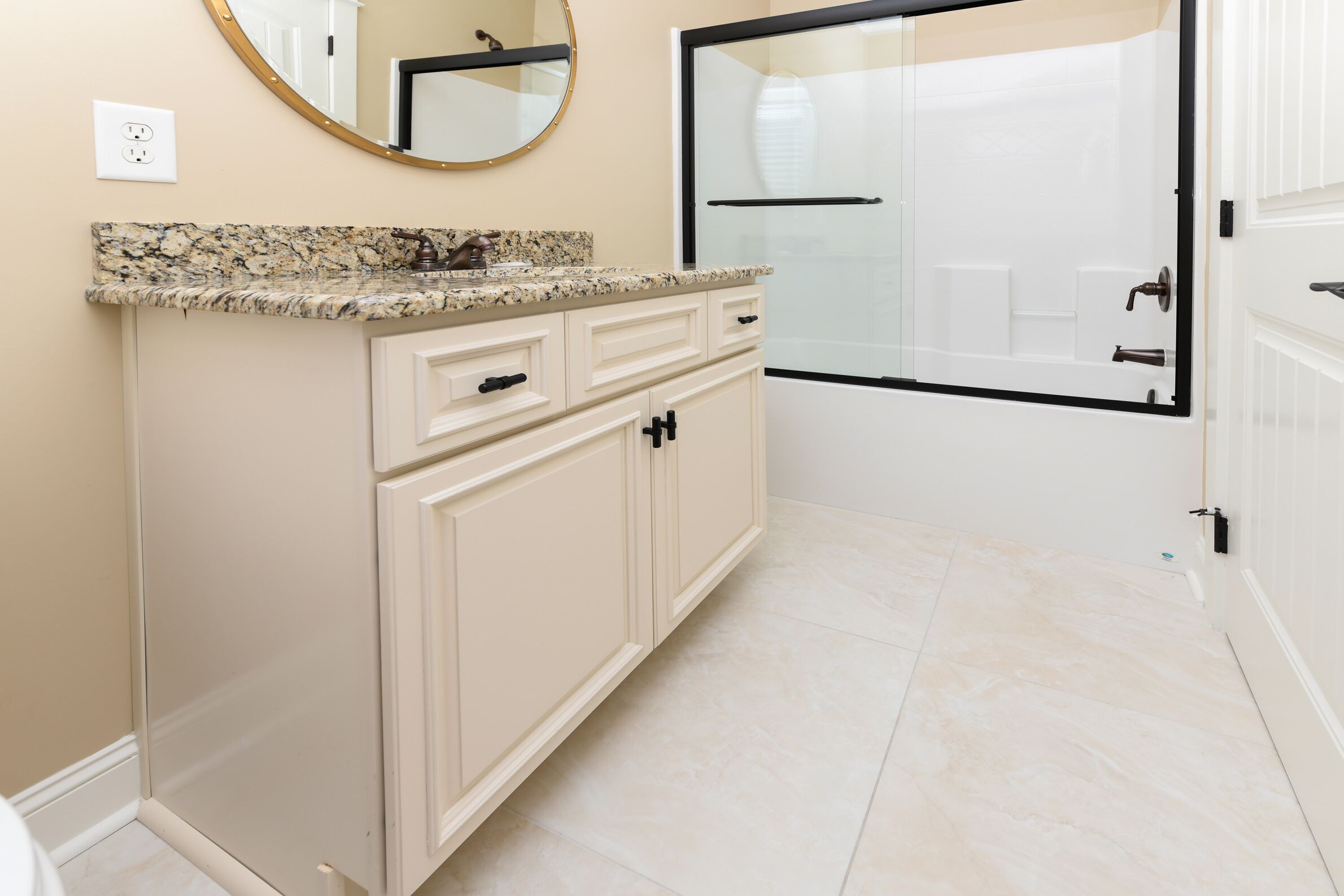 A bathroom with a granite countertop, a sink, a mirror, a shower with a glass door, and beige cabinetry.