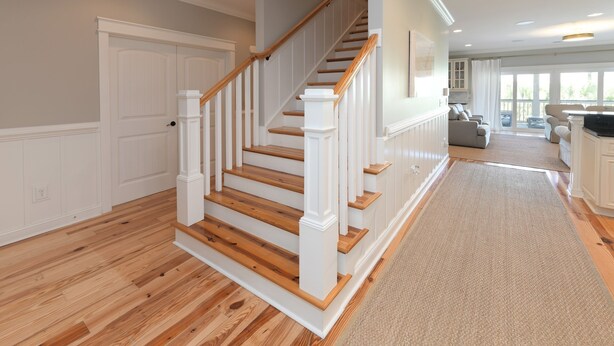 Un escalier avec des rampes blanches et des marches en bois, menant à un palier doté d’une porte.
