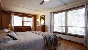 A bedroom with a bed, a desk, and a chair. There is a window with curtains and a view of trees outside. - Great Fishing, Gorgeous Views, Private Cabin on Pelican Lake (Orr)