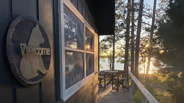 A wooden deck with a 'Welcome' sign, overlooking a lake with trees in the background. - Great Fishing, Gorgeous Views, Private Cabin on Pelican Lake (Orr)