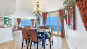 Une salle à manger spacieuse avec vue sur la mer, un lustre et un balcon agrémenté de rideaux.