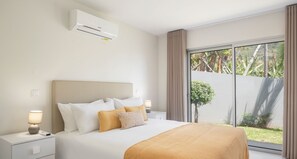 Relax in a serene space with a large bed, bedside table, and sliding glass door to an outdoor area with lush greenery.