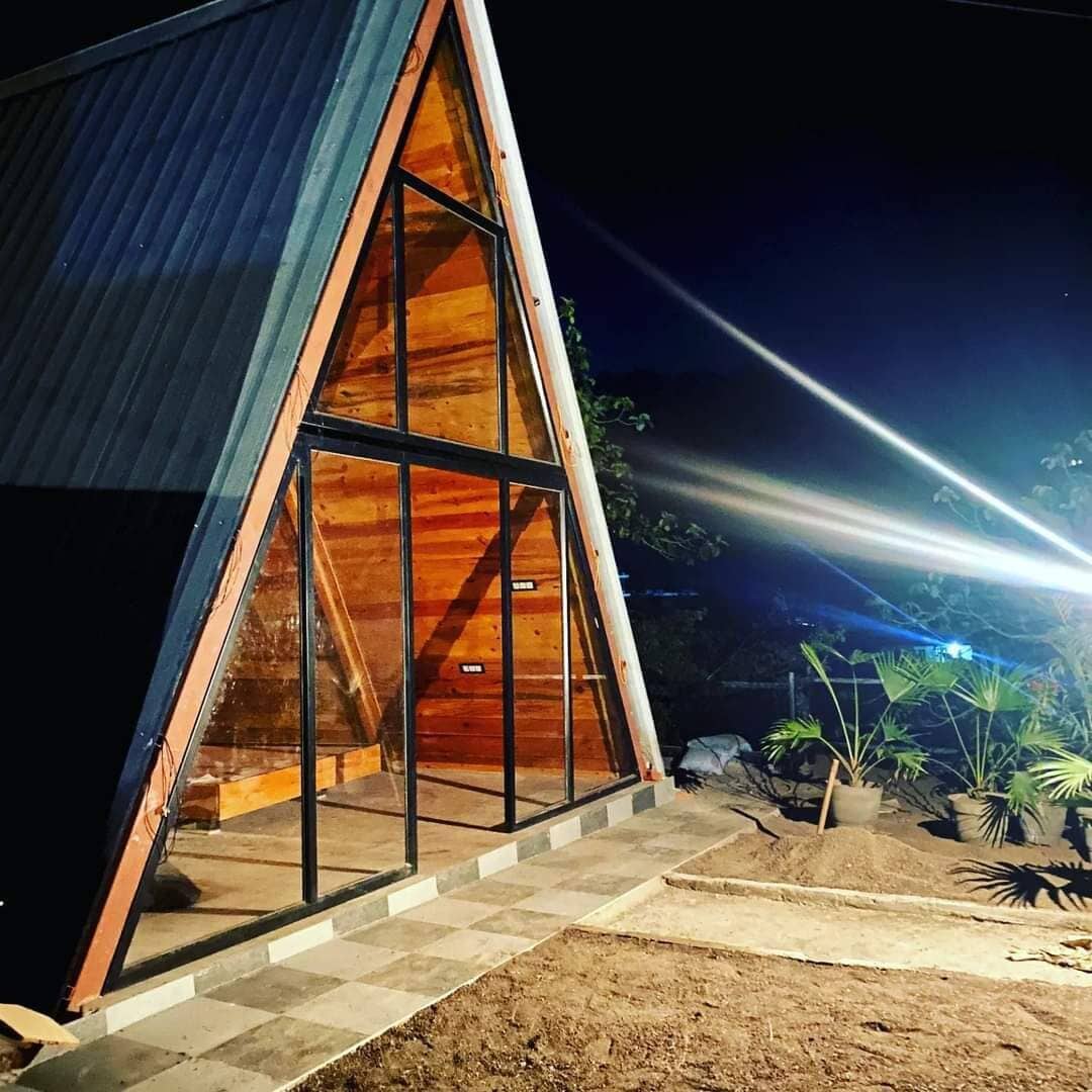 Una estructura de madera triangular con amplios ventanales, rodeada de un área pavimentada y plantas en macetas.