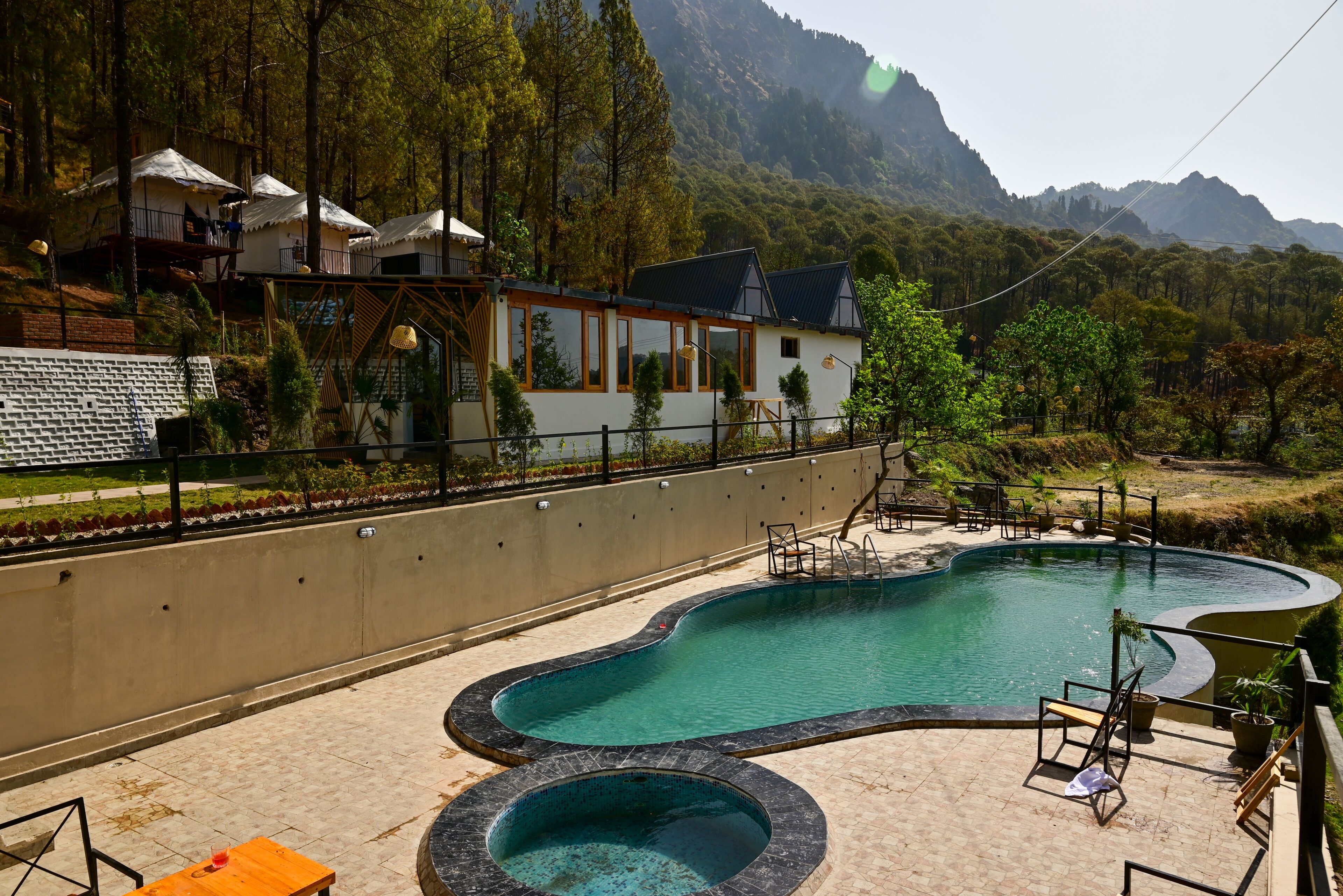 Un área de piscina con un jacuzzi, sillones de descanso y vistas a un paisaje montañoso.