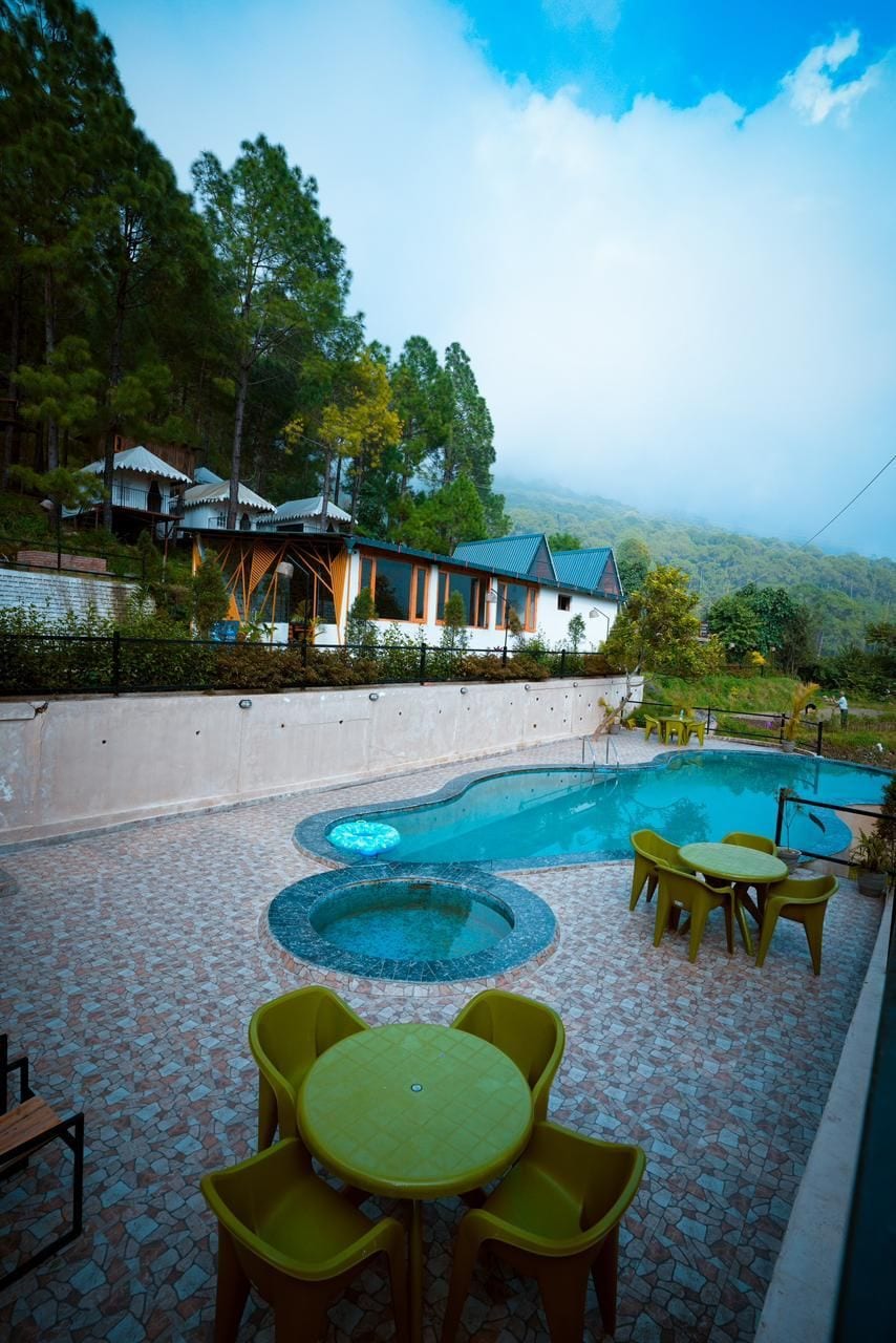 A pool area with a circular hot tub, yellow chairs, and a view of a house with a green roof.
