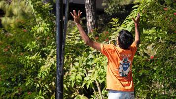 Un aro de baloncesto con red, un balón de baloncesto en pleno vuelo, y una persona con camiseta naranja y vaqueros alcanzando la pelota.