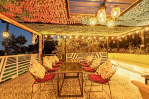 An outdoor seating area with a long table and chairs, surrounded by a decorative ceiling and string lights. - Paradise Pool Resort (Nainital)