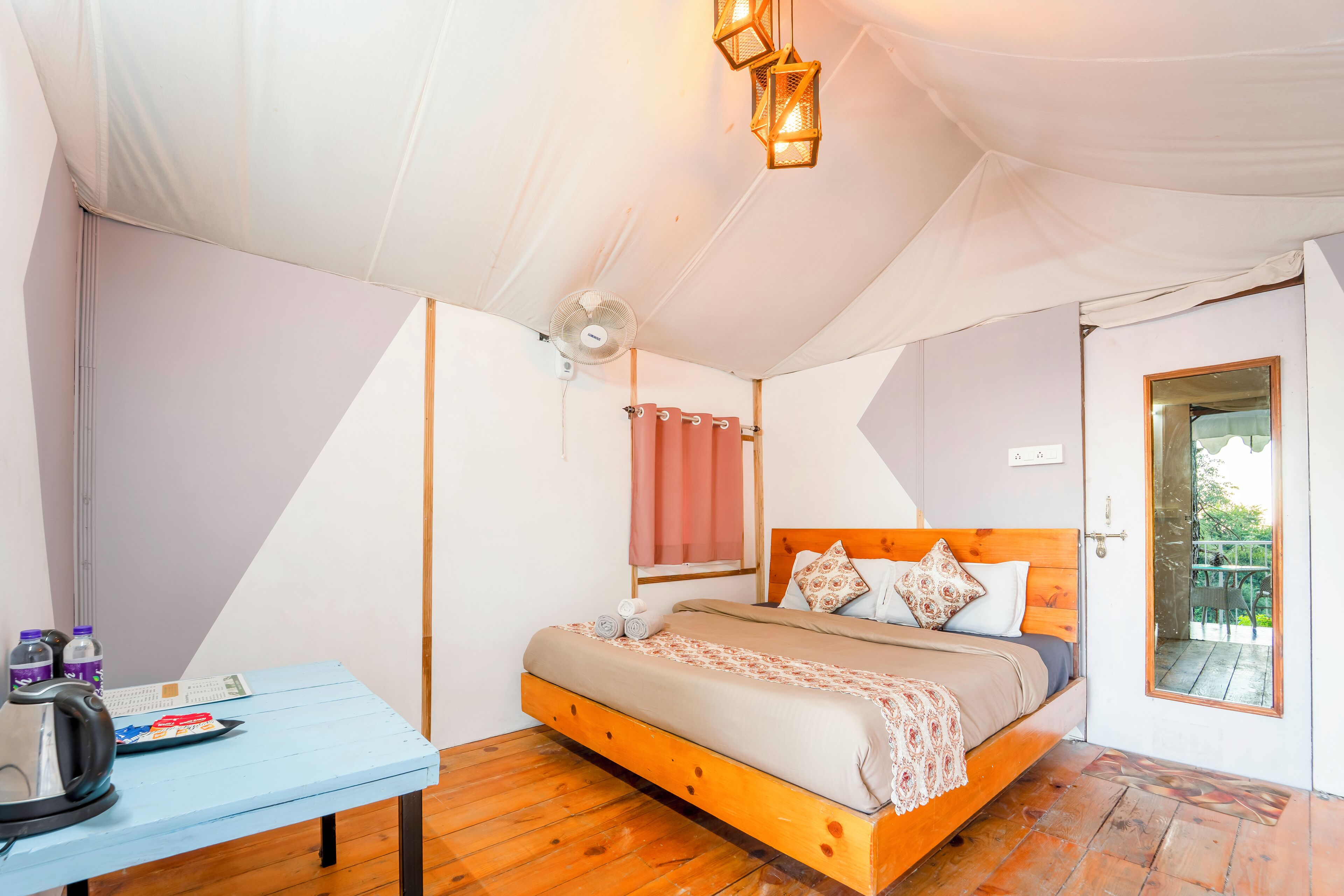 A bedroom with a bed, a table with a kettle, and a fan.