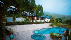A resort with a swimming pool, outdoor seating, and multiple bungalow-style accommodations surrounded by lush greenery. - Paradise Pool Resort (Nainital)