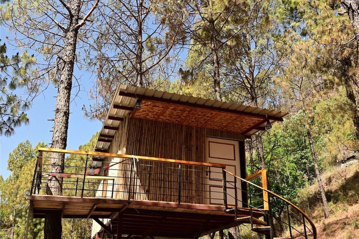 A wooden cabin with a balcony, a staircase, and a white tent in the background.