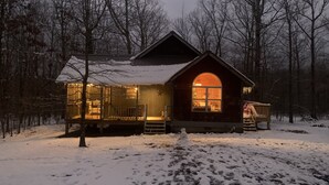 A cozy cabin with a porch, a snow-covered yard, and a large window. - ⭐️Glory Days Cottage⭐️ Cozy/Quiet/Serene🏡 (Mentone)