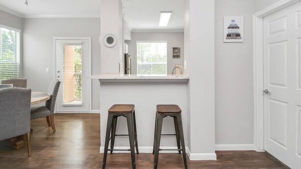 A modern kitchen with a white countertop, two stools, and a dining area with a table and chairs.