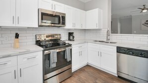 A modern kitchen with white cabinets, stainless steel appliances, and a wooden floor.