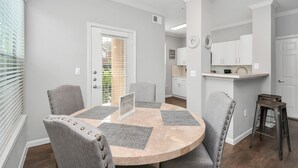 A dining area with a round table, four chairs, and a kitchen in the background.