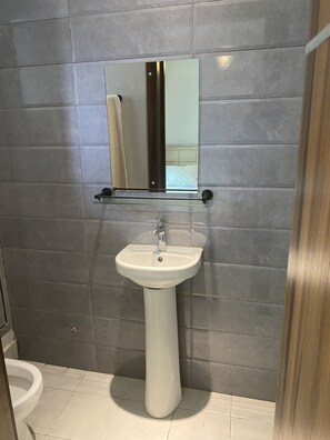 Un bagno con lavabo a piedistallo, uno specchio sopra e pareti rivestite di piastrelle grigie.