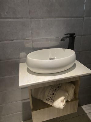 A bathroom with a white oval sink, a black faucet, and a wooden shelf with a towel.