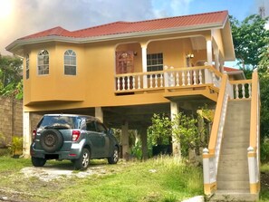 A two-story house with a balcony, a car parked in front, and a staircase leading to the upper level.