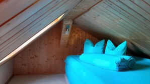 A small, cozy attic bedroom with a sloped ceiling, wooden walls, and a single bed with pillows. - Quiet vacation home with garden (Lichtenstein/Sa.)