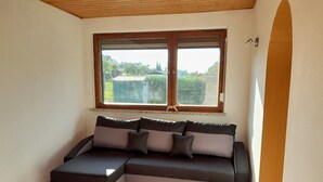 A room with a sectional sofa, a large window, and a wooden ceiling. - Quiet vacation home with garden (Lichtenstein/Sa.)