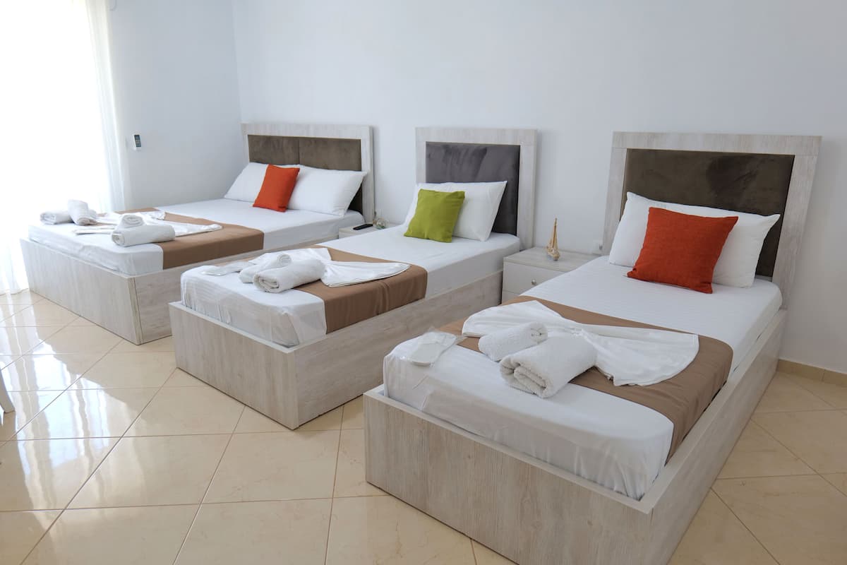 Three single beds with wooden headboards, white linens, and colorful pillows.