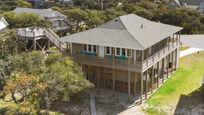 A two-story wooden house with a balcony and a deck, surrounded by trees and other houses. - Canalfront Dog Friendly Home in Frisco with Elevator and Private Boat Dock (Frisco)