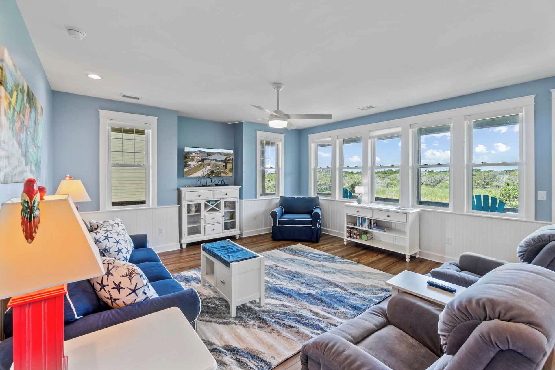 A spacious living room with a large window, a ceiling fan, and a television on the wall.