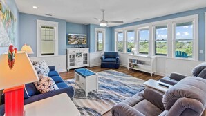 A spacious living room with a large window, a ceiling fan, and a television on the wall. - Canalfront Dog Friendly Home in Frisco with Elevator and Private Boat Dock (Frisco)