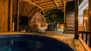Un espace aménagé au bord de la piscine, comprenant un fauteuil suspendu, un coin salon couvert et une piscine.