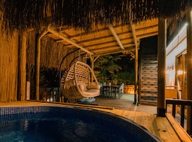 A poolside area with a hanging chair, a covered seating area, and a pool.