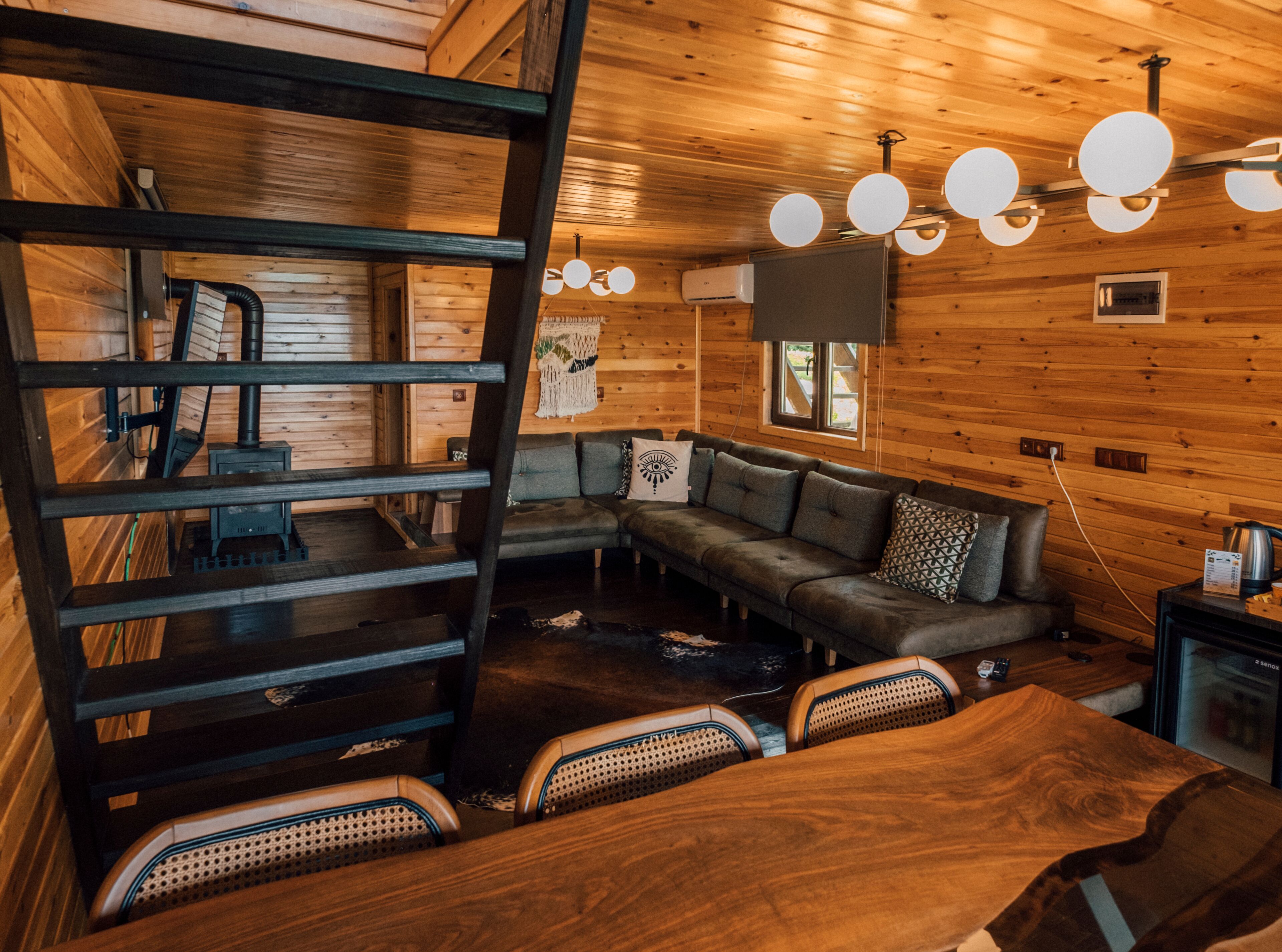 Ein gemütliches Blockhaus-Interieur mit Holzausstattung, einer Couch, einem Esstisch und einer Wendeltreppe.