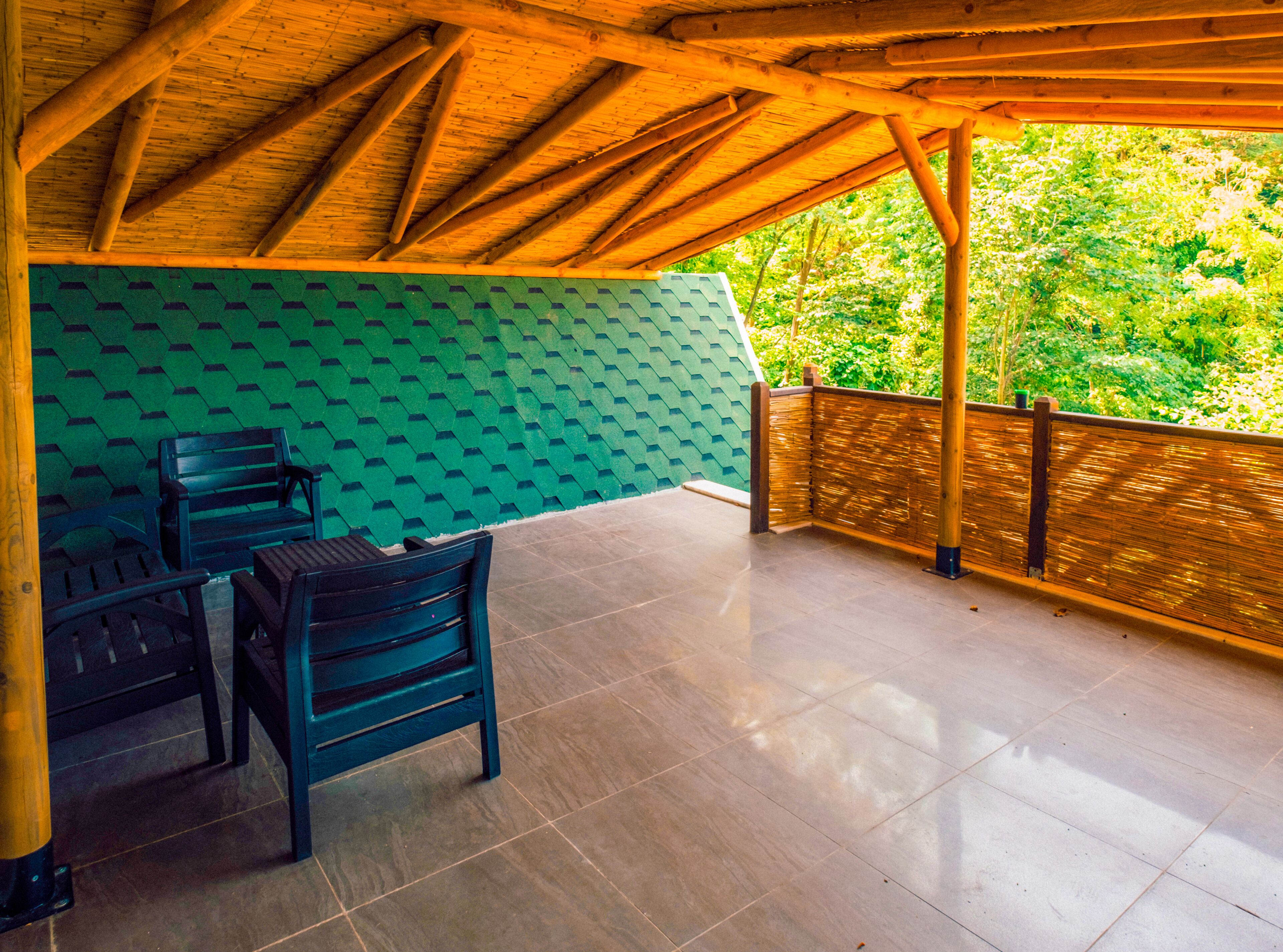 Un espacio de estar al aire libre cubierto con vigas de madera, paredes de patrón verde y vistas a abundante vegetación.