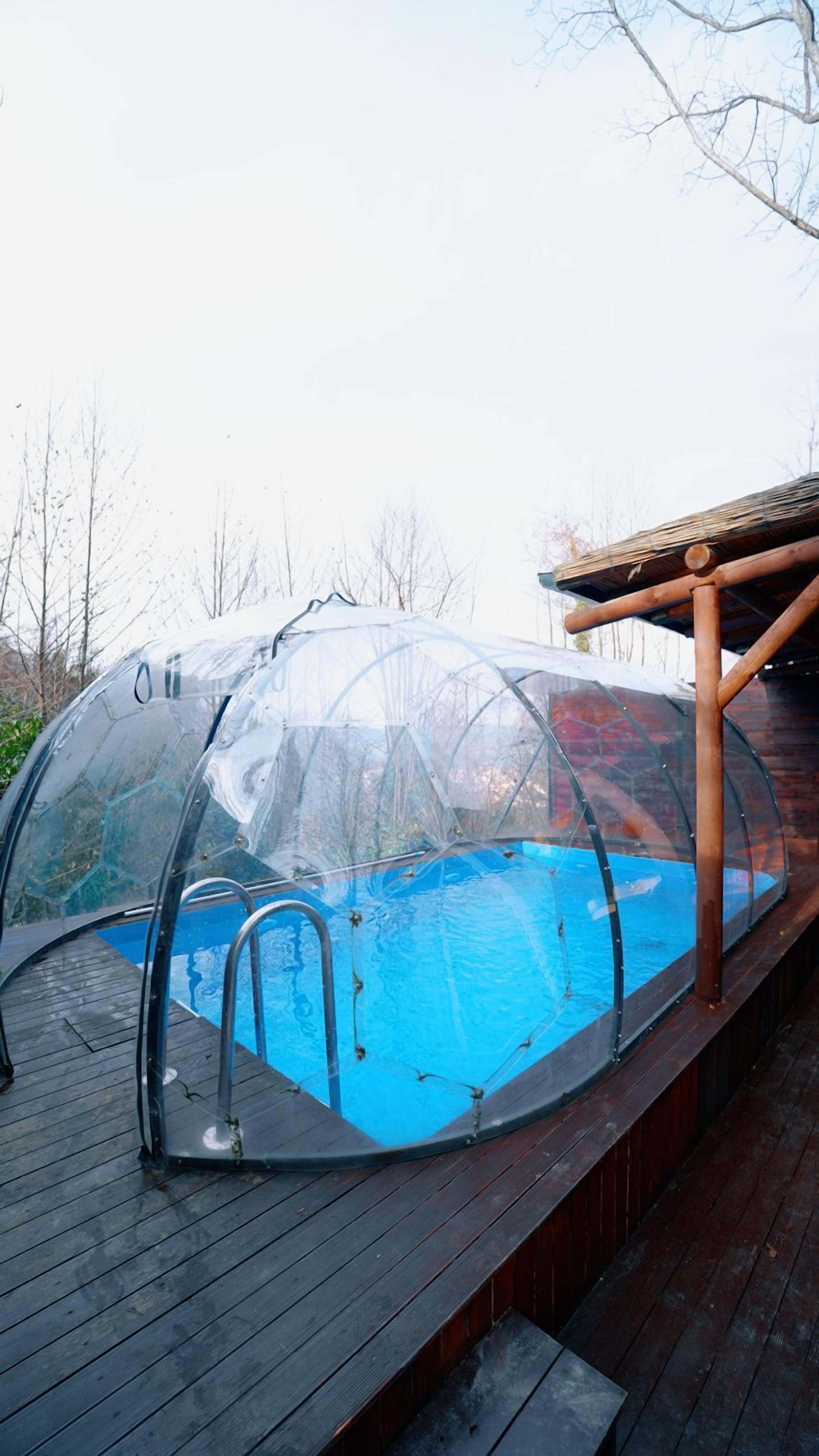 A transparent swimming pool with a wooden deck and a covered area.