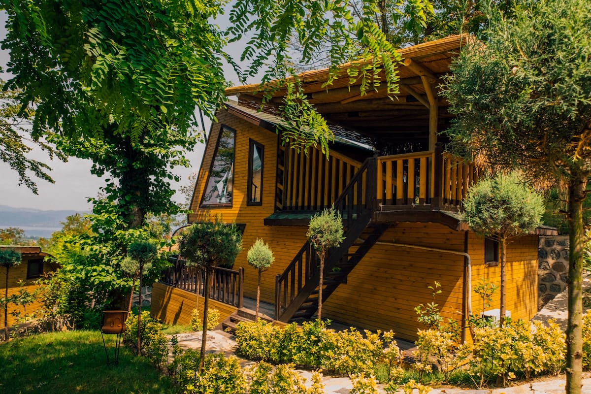 Een houten huis met een stenen fundering, een houten terras en een trap naar een tweede verdieping.