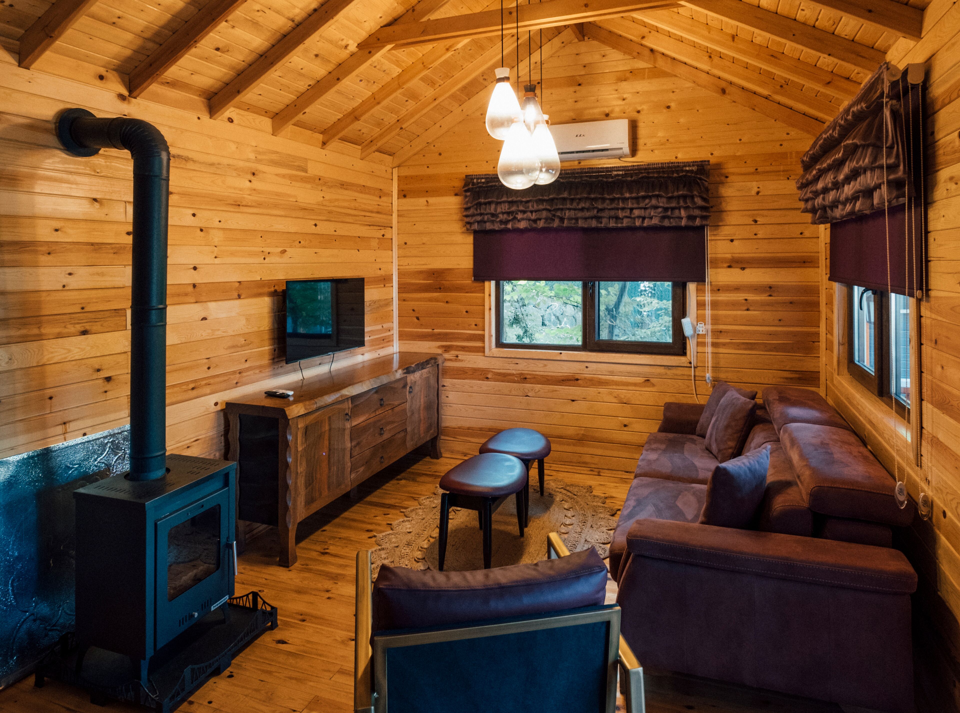 A cozy cabin interior with a wooden interior, a fireplace, a sofa, and a television.