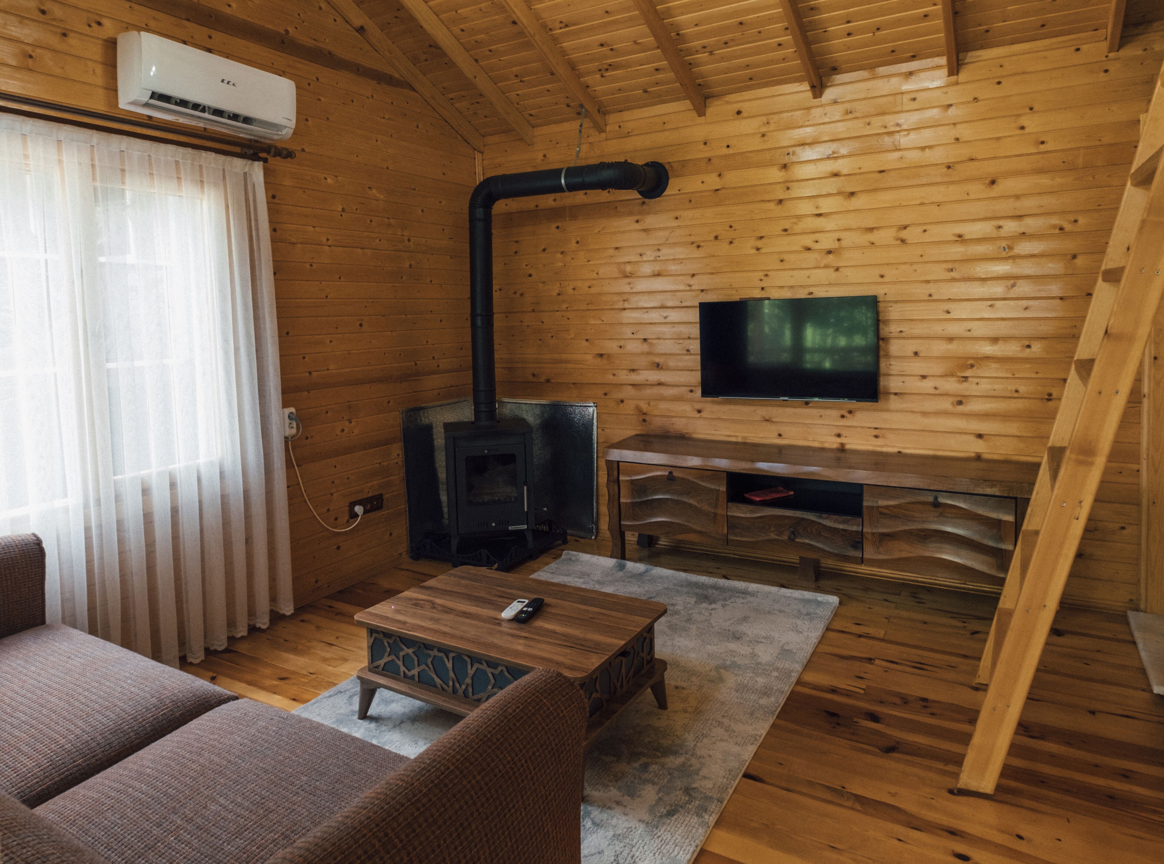 Un acogedor interior de cabaña de madera con chimenea, un televisor montado en la pared y una zona de estar confortable.
