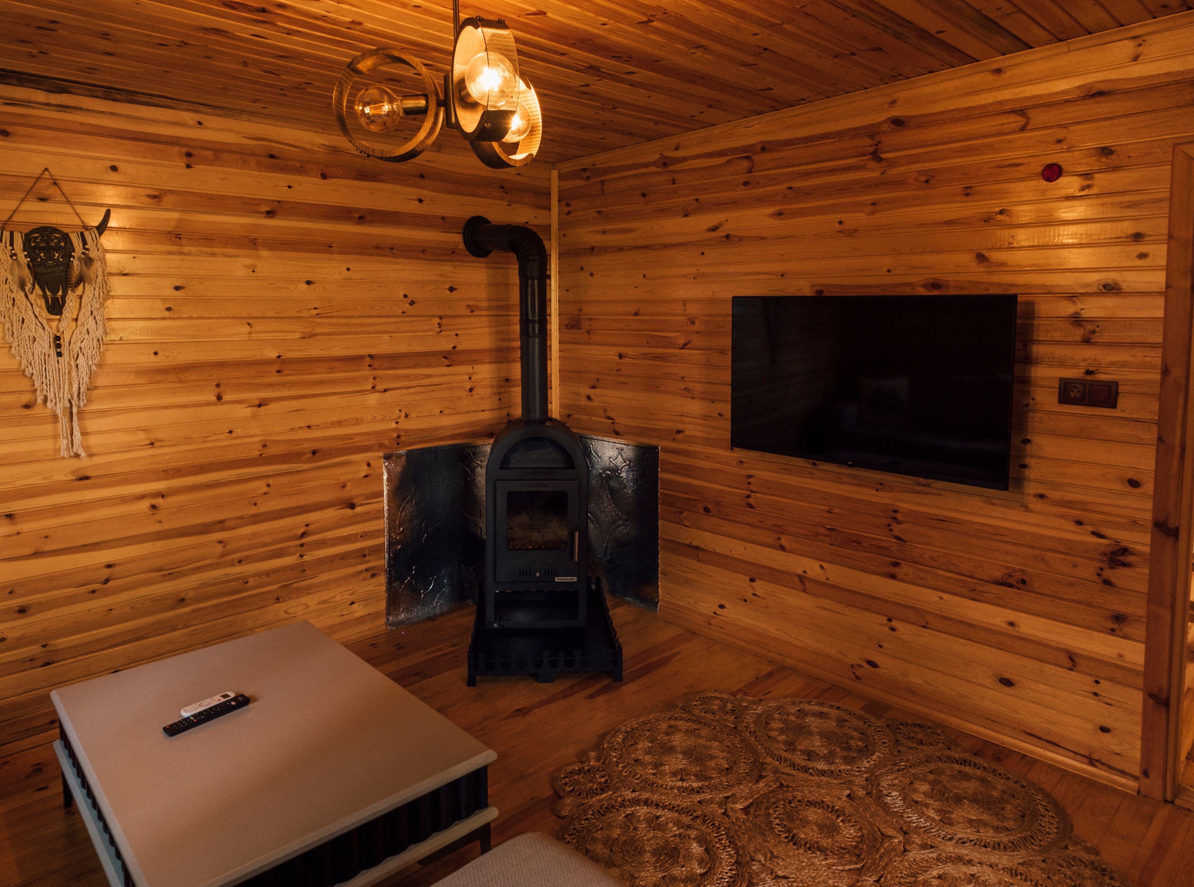 Ein gemütliches Holzhaus-Interieur mit Kaminofen, Fernseher und Fernbedienung auf einem Tisch.