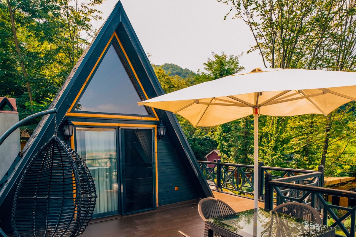 Een gebouw in driehoekige vorm met een glazen deur, terras met een tafel en stoelen, en een parasol.