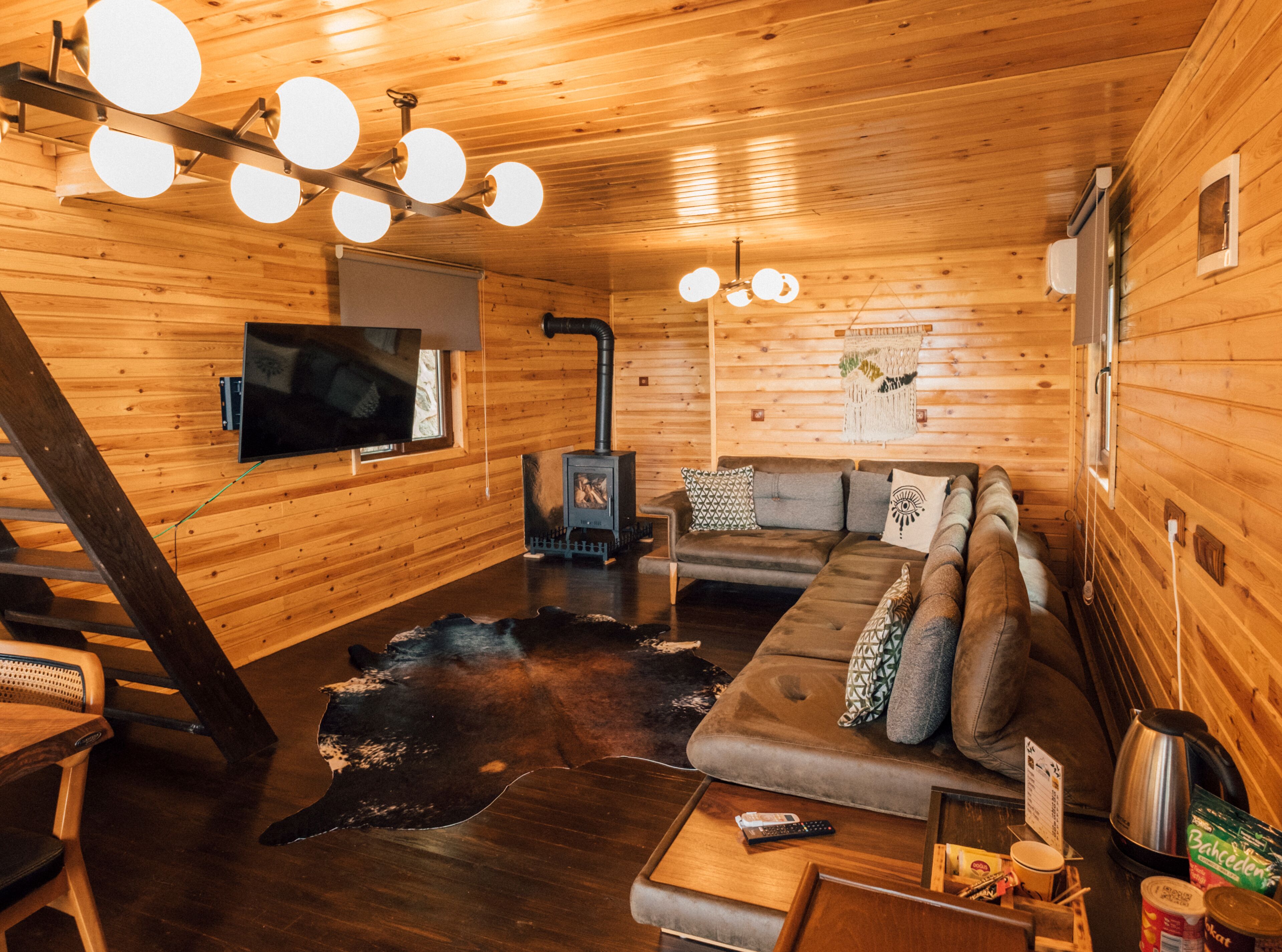 A cozy cabin interior with a wooden interior, a sofa set, a television, a fireplace, and a staircase.