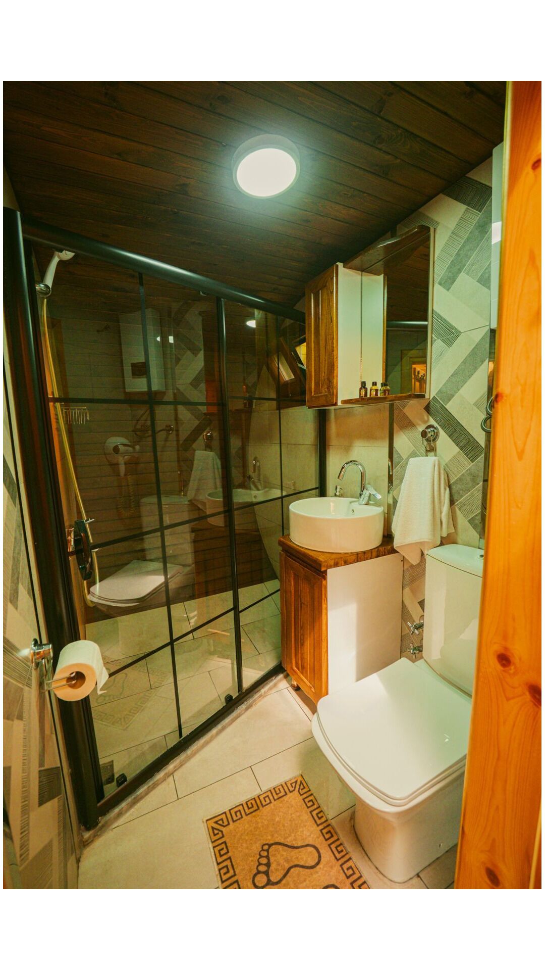 A bathroom with a glass shower enclosure, a wooden vanity, a white sink, and a toilet.