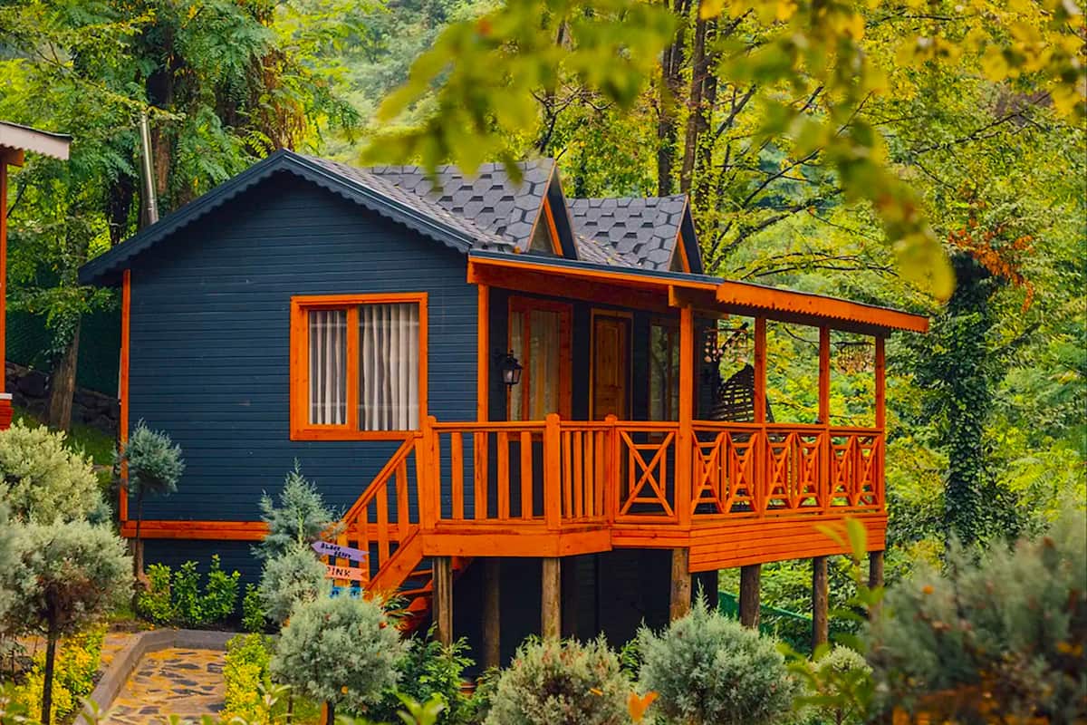 Een houten chalet van twee verdiepingen met een balkon, omgeven door weelderige begroeiing.