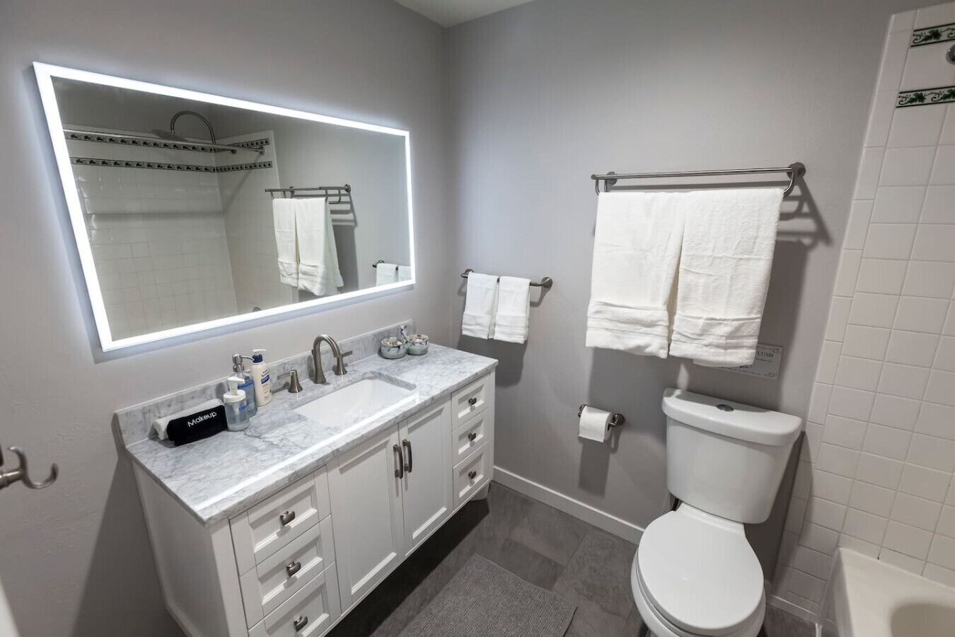 A modern bathroom with a large mirror, a sink, a toilet, and a shower area.