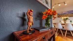 Eine Statue auf einem Holztisch, eine Vase mit orangefarbenen Blumen und ein Essbereich mit Stühlen und Tisch.