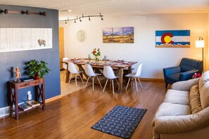 A living room with a wooden dining table, white chairs, a blue sofa, and a rug. - Private btwn Boulder & Denver, Mountains Game Room (Westminster)
