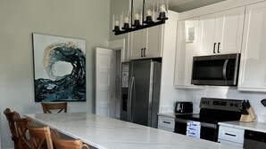 A modern kitchen with a large island, white cabinetry, stainless steel appliances, and a wooden chair arrangement.
