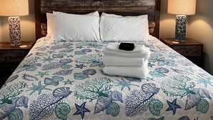 A bed with a nautical-themed bedspread, two bedside tables with lamps, and a wooden headboard.