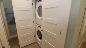 A laundry room with a front-loading washer and dryer, wooden flooring, and white doors.