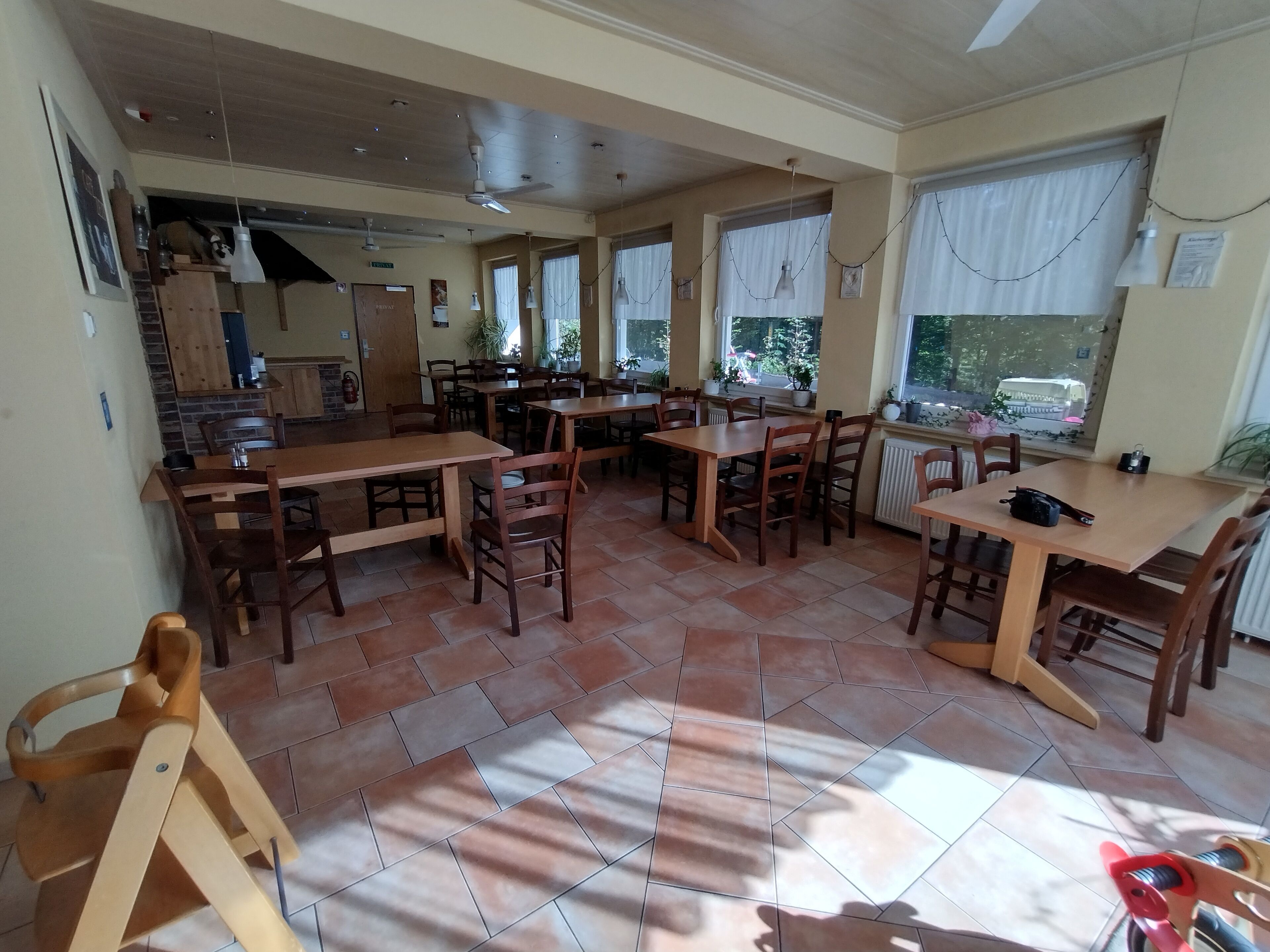 Ein geräumiger Essbereich mit mehreren Holztischen und Stühlen, großen Fenstern mit Vorhängen und einem Deckenventilator.