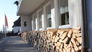 Un edificio con leña apilada afuera, una bandera y un sendero pavimentado.