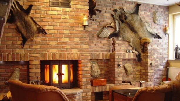 Una habitación acogedora con chimenea de ladrillo, sillones de cuero y monturas de animales en la pared.