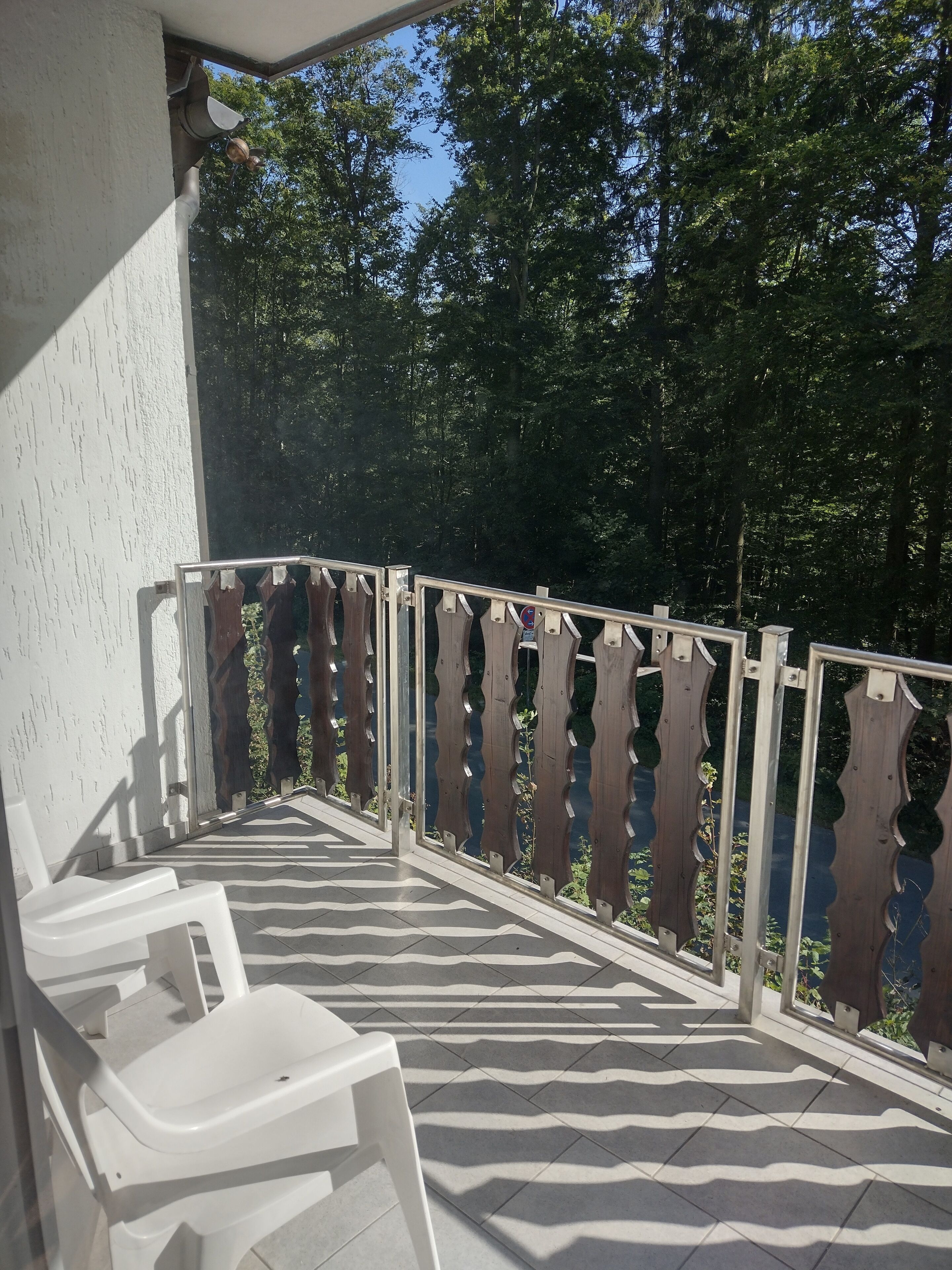 Ein Balkon mit einem gemusterten Boden, weißen Plastikstühlen und einem Metallgeländer mit Verzierungen.